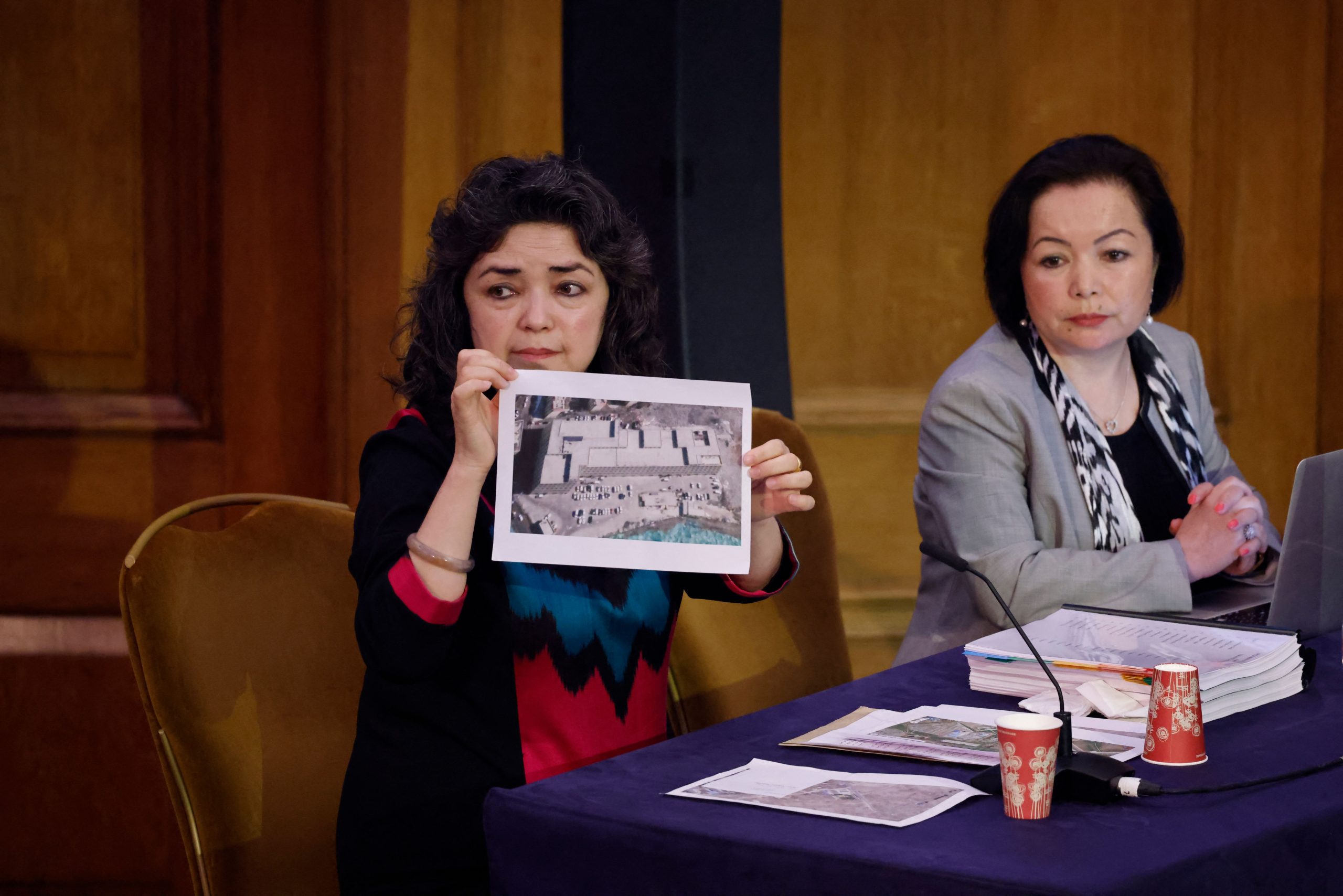 A Uyghur woman holds up a photograph as evidence in a wood paneled room in London