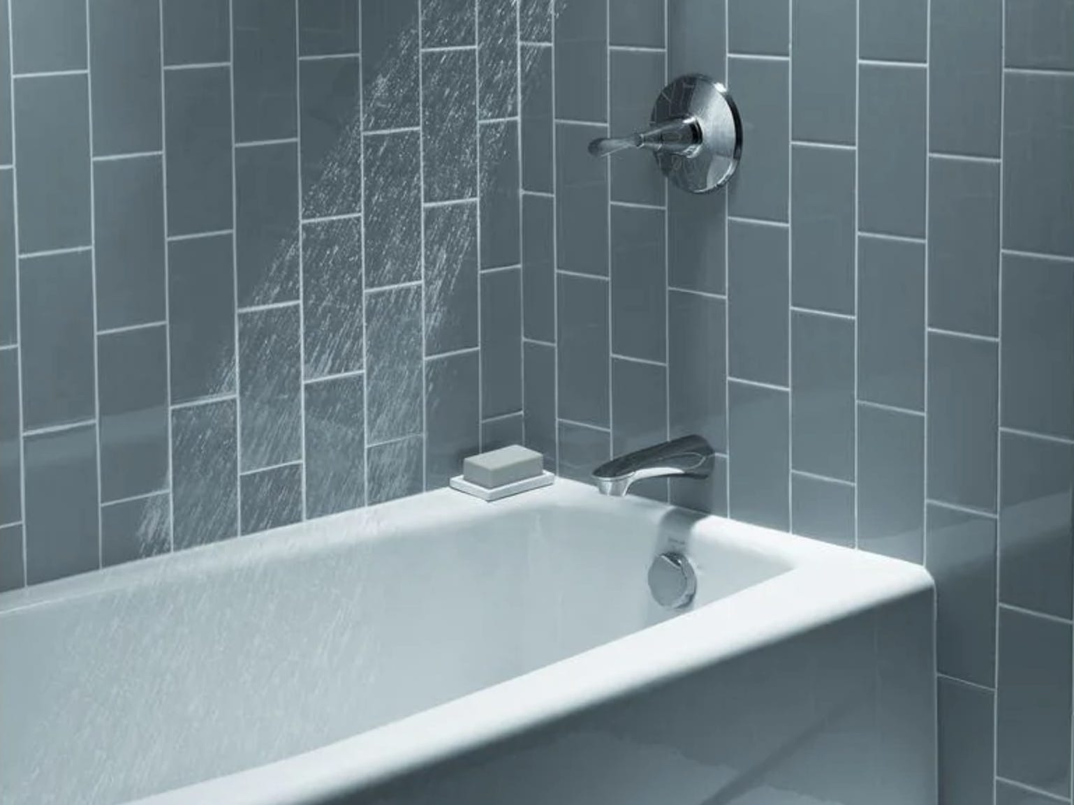 A closeup of a tub in a tiled shower with the water falling from the showerhead