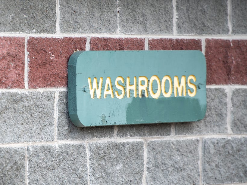 a washroom sign with yellow letters on a green background in a park